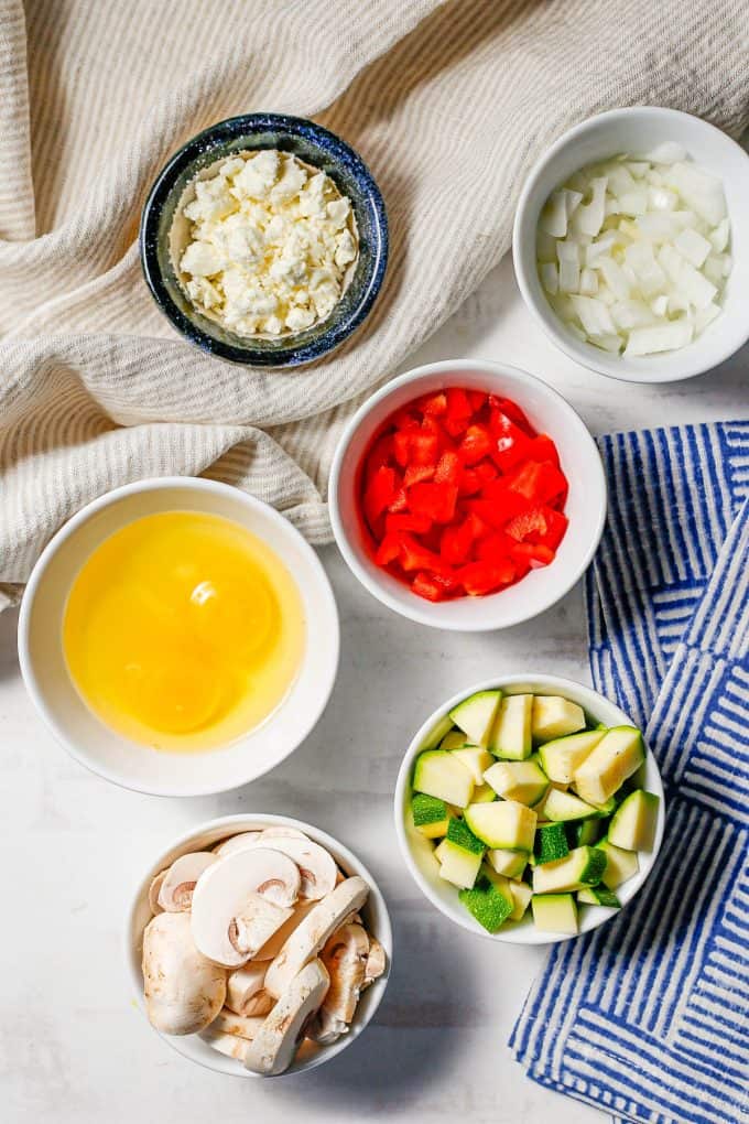 Ingredients laid out in separate bowls for an egg scramble with veggies.