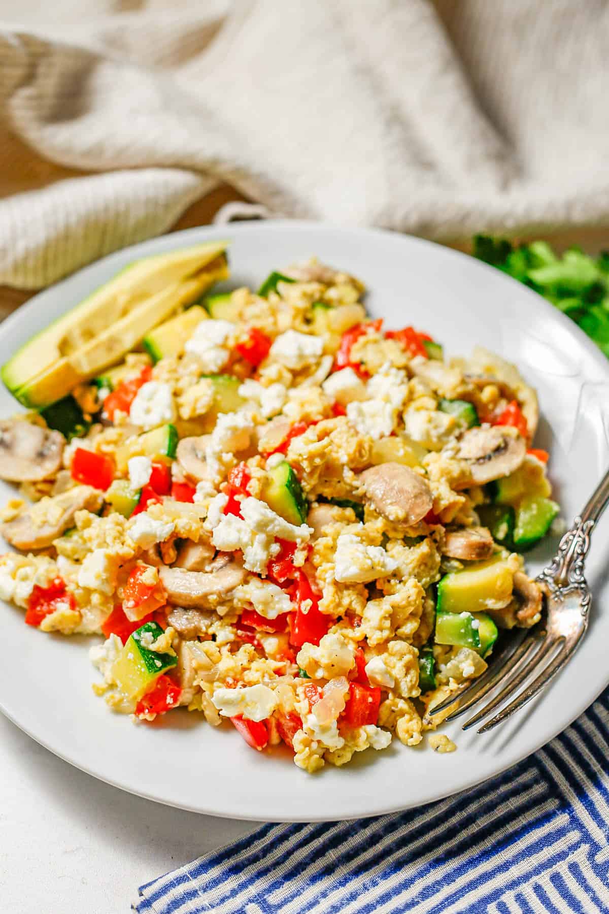 A white plate with an egg veggie scramble mixture topped with feta cheese and a fork resting on the plate.