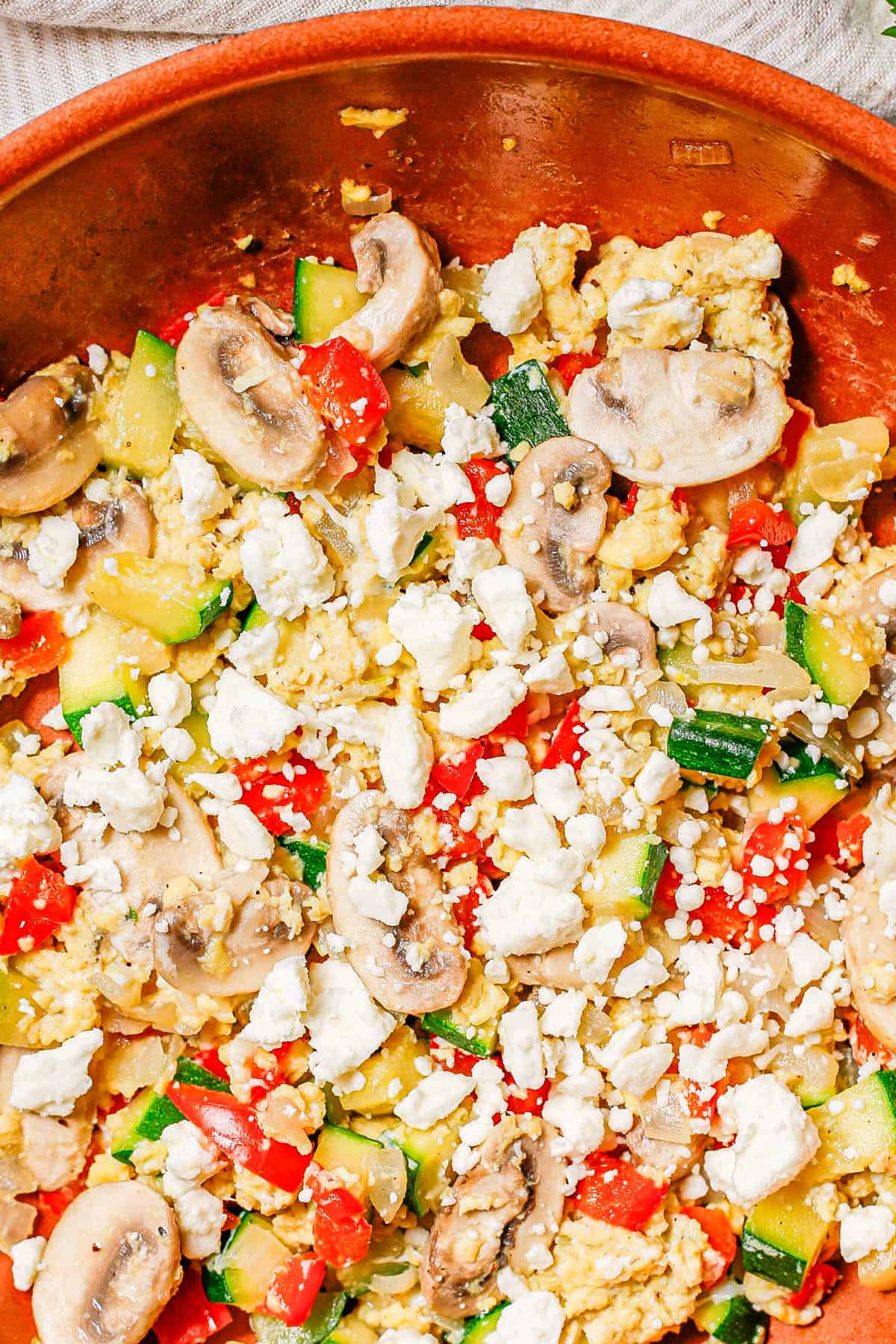 Close up of an egg veggie scramble mixture in a copper skillet with feta cheese on top.