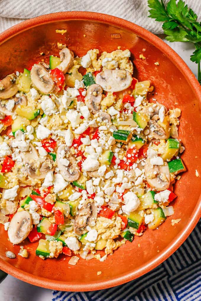A mix of scrambled eggs and sautéed veggies in a copper skillet with feta cheese on top.