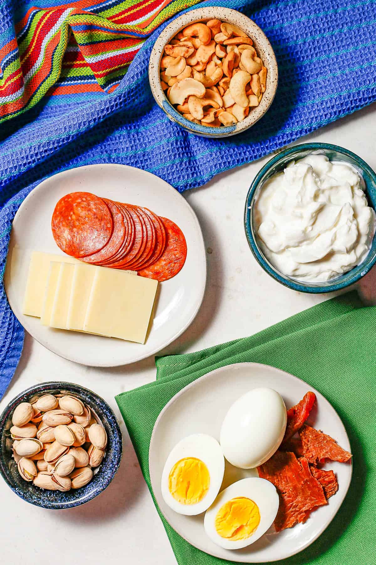 Plates and bowls of different high protein snacks laid out on a counter with colorful napkins.