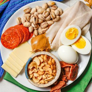 Close up of a plate of high protein snacks, including nuts and cheese and hard boiled eggs.