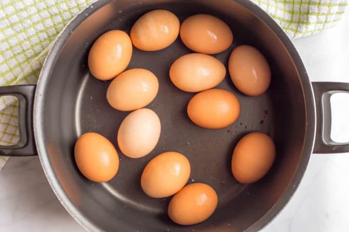 A large dark pot with a dozen hard boiled eggs in it.