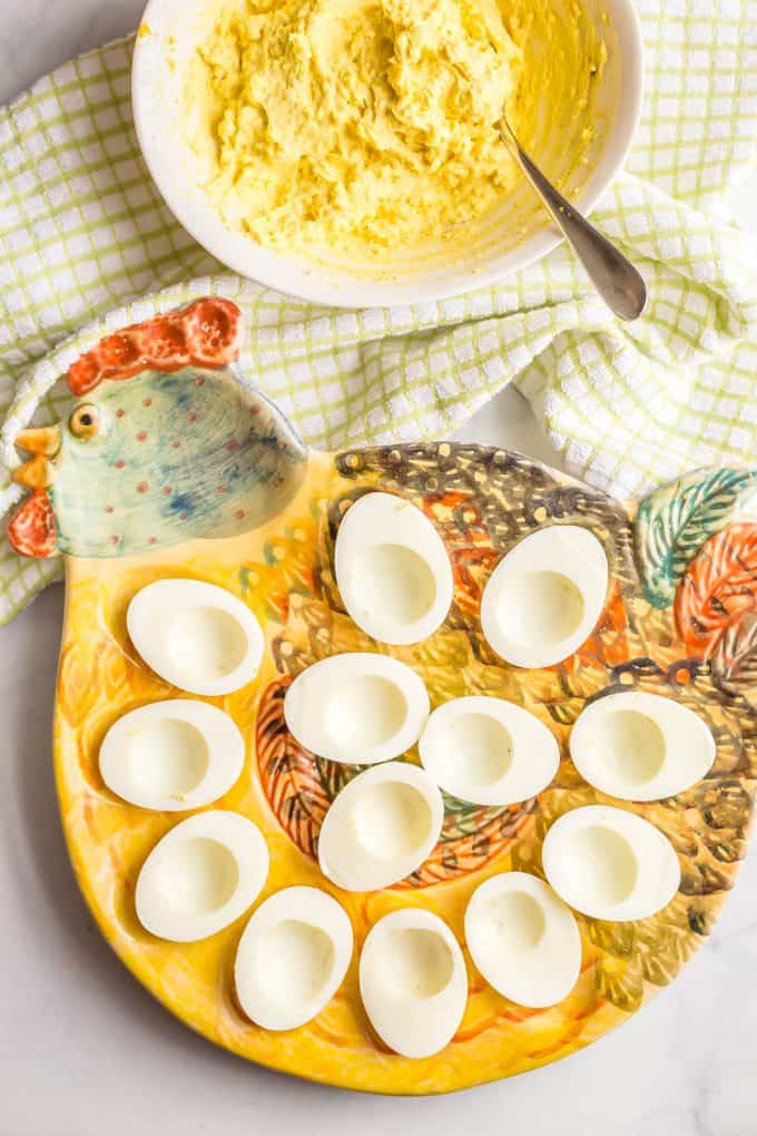 A rooster plate with halved, emptied egg whites with a deviled egg filling mixture in a bowl to the side.