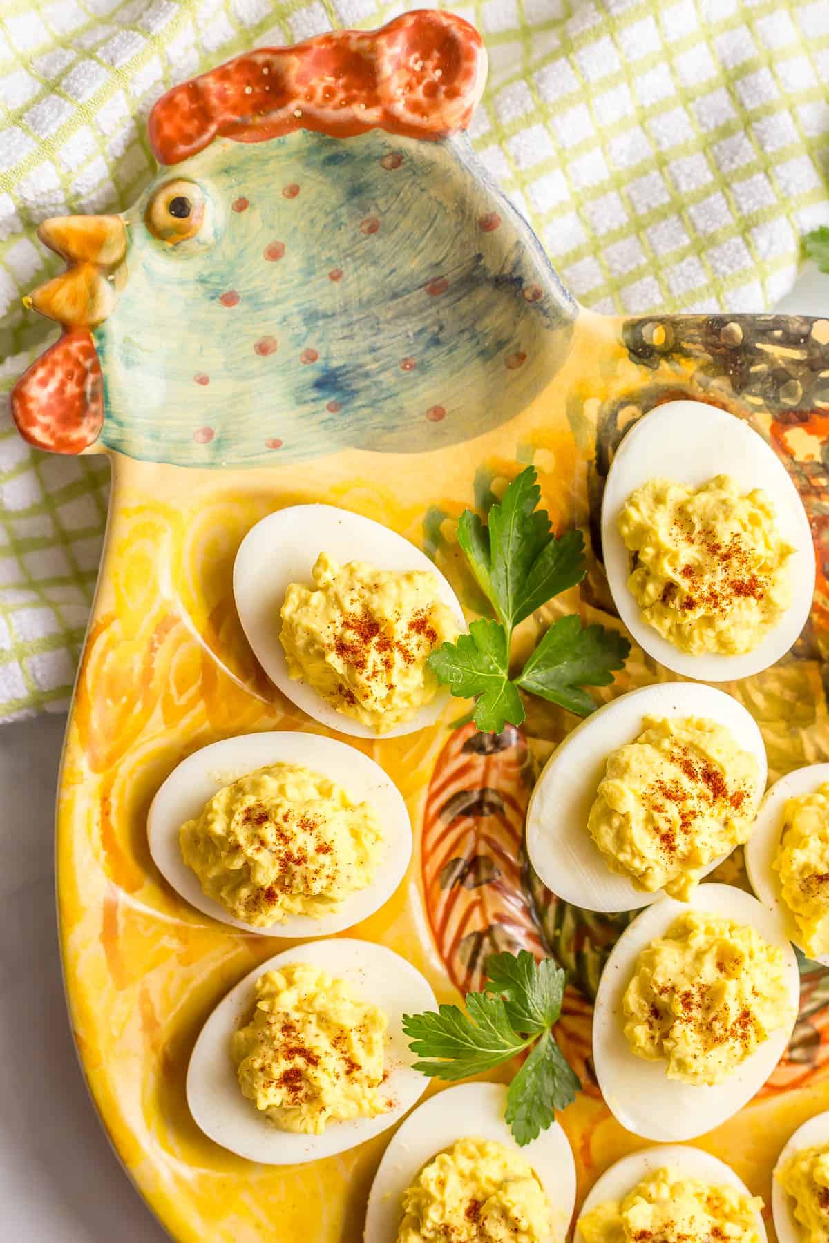 Close up of deviled eggs on a rooster egg plate with paprika sprinkled on top and sprigs of parsley for garnish.