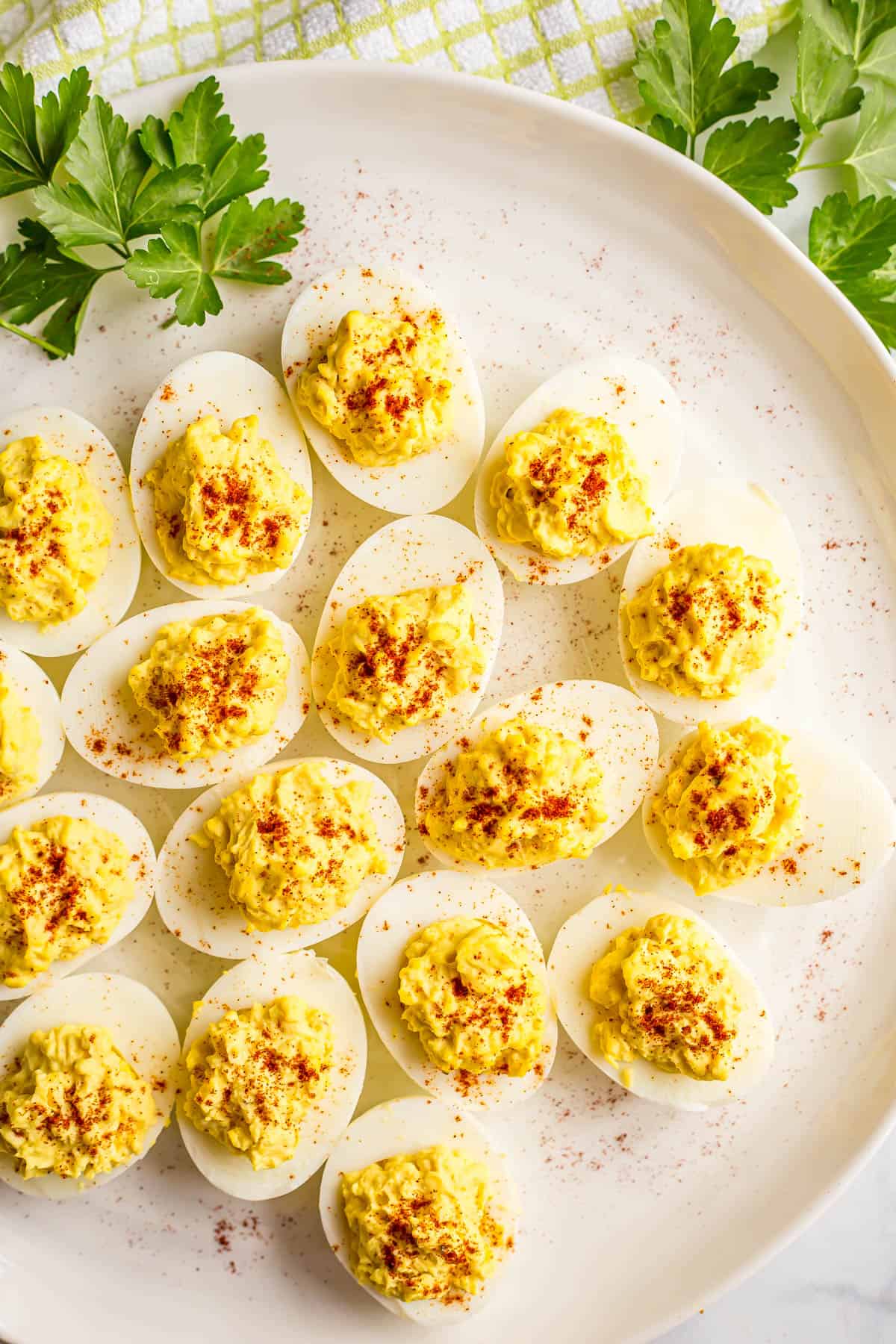 A white round platter with Southern deviled eggs and parsley sprinkled on top with sprigs of parsley to the side.