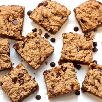 Square bars of a peanut butter chocolate chip snack on a white platter with chocolate chips scattered around.