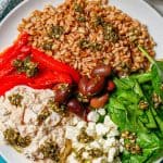 Close up of an arranged salmon grain bowl with veggies, feta and olives and a drizzle of pesto over everything with a text overlay on the photo.