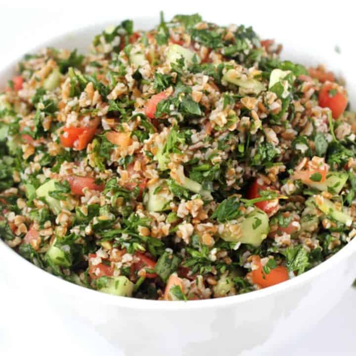 Close up of a tabbouleh salad with fresh herbs and tomatoes and cucumbers served in a large white bowl.