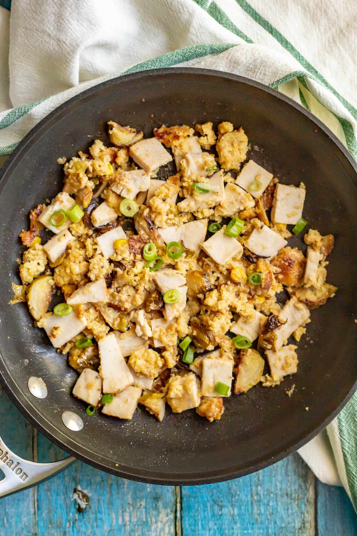 A large skillet with a mixture of leftover turkey, dressing and veggies with green onions on top.