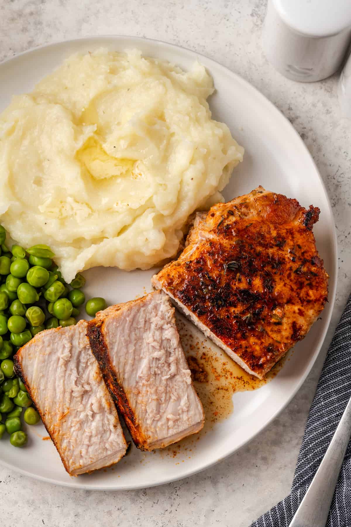 A sliced pork chop alongside buttery mashed potatoes and peas on a dinner plate.