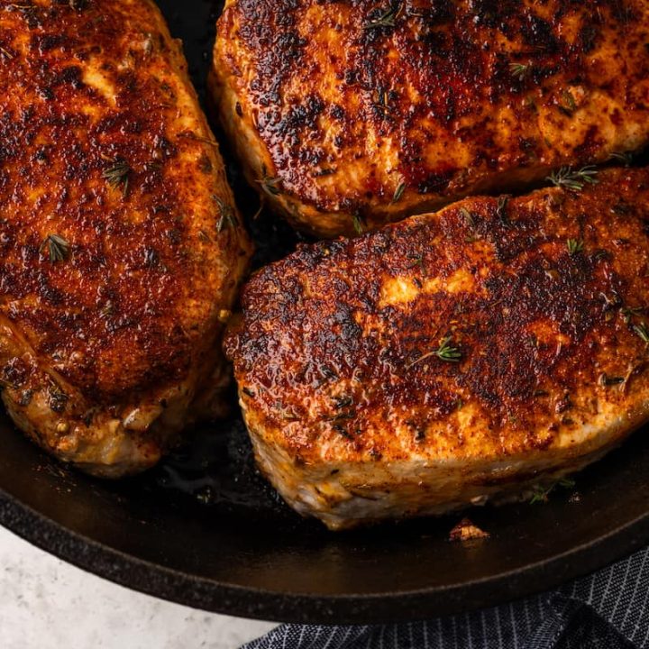 Close up of seared and cooked seasoned pork chops in a cast iron skillet.