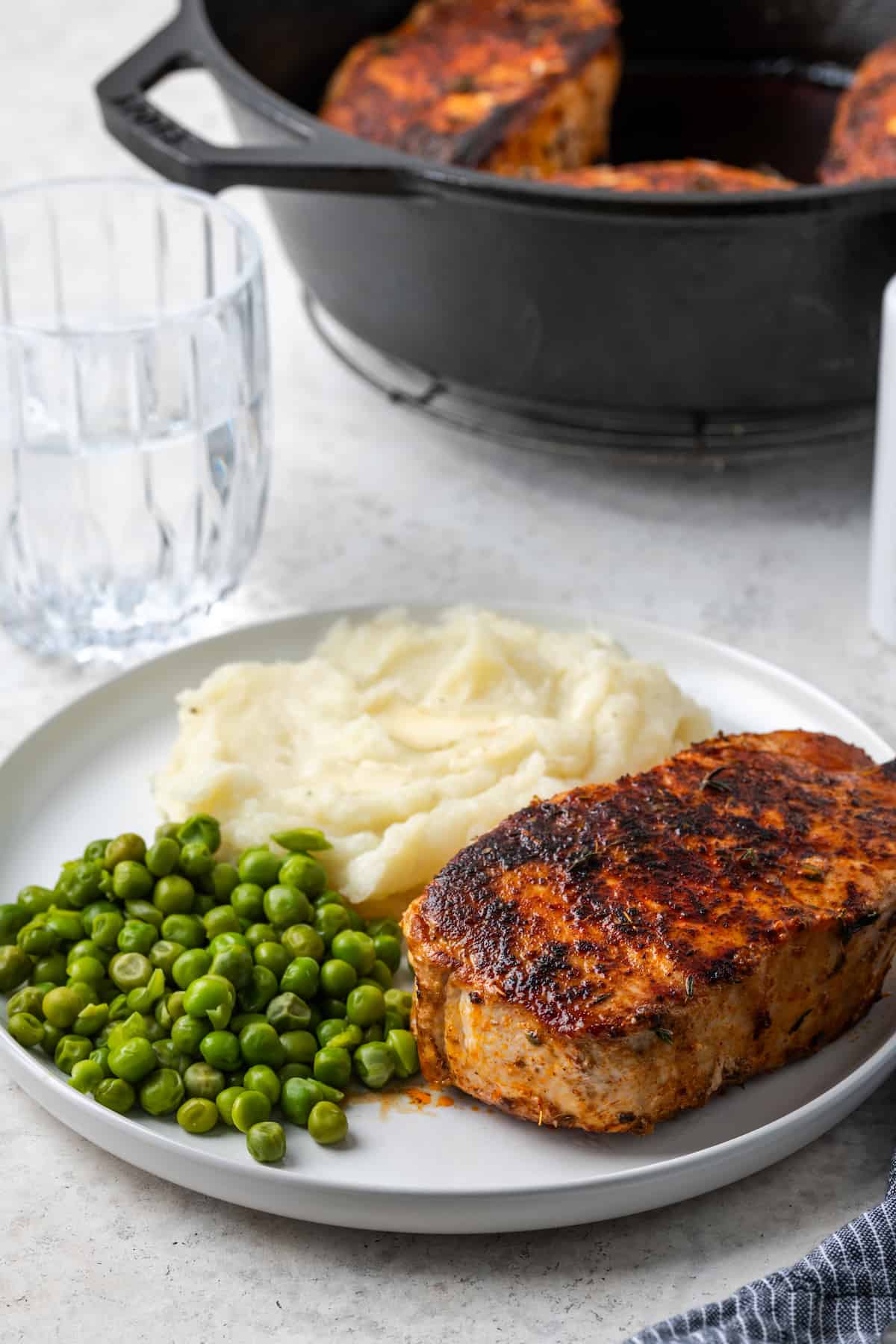 A dinner plate with a seared and seasoned pork chop alongside peas and mashed potatoes.