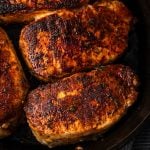 Close up of seared and cooked spice rubbed pork chops in a cast iron skillet with a text overlay on the photo.