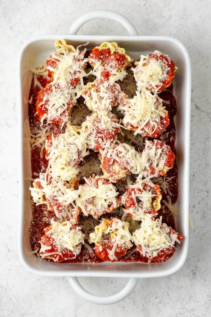 A large white casserole dish with marinara sauce in the bottom, rolled up veggie lasagna rolls and cheese and marinara spread over top.