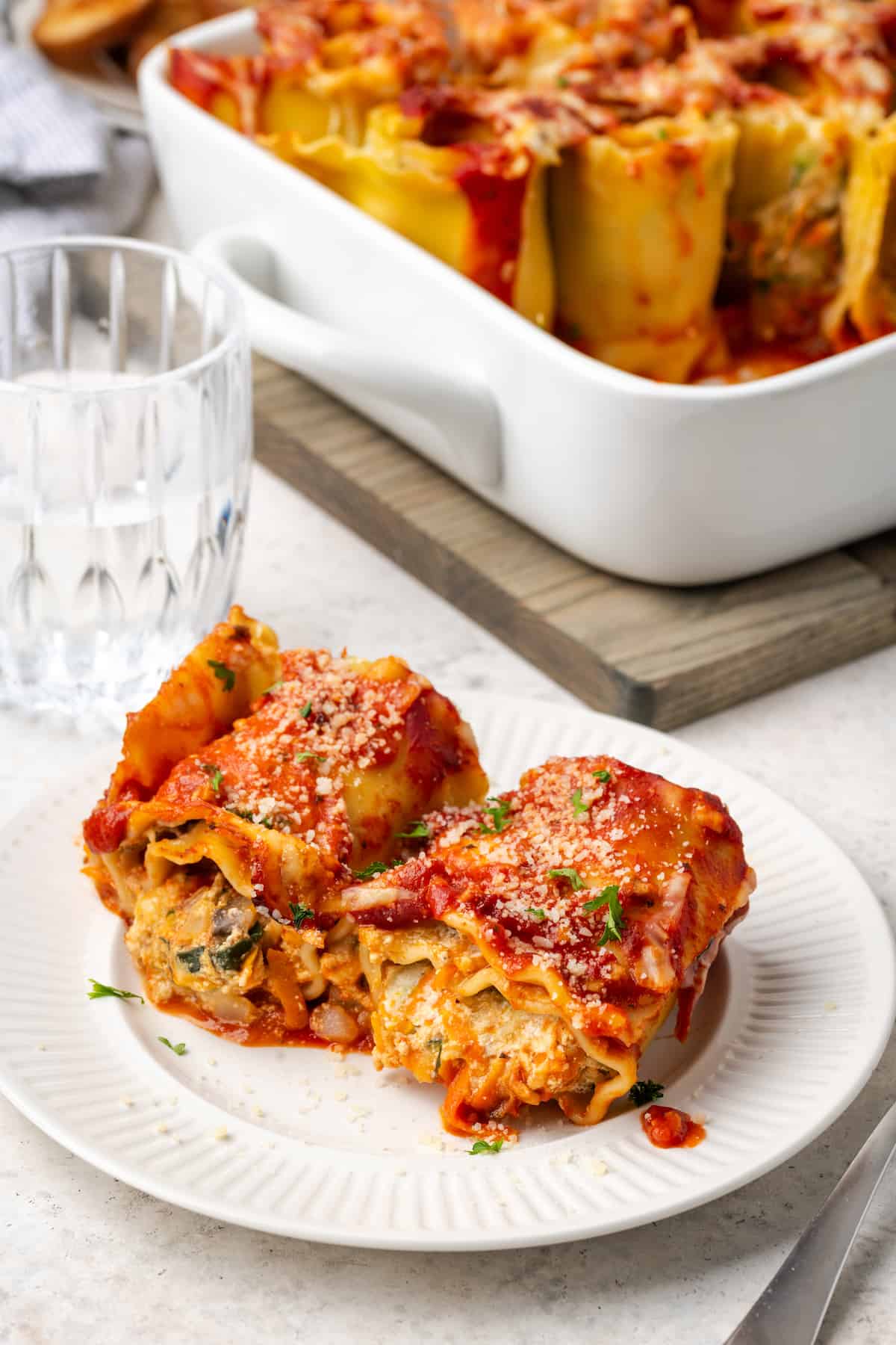 Two veggie lasagna roll ups served on a small white plate with the remaining casserole dish in the background.