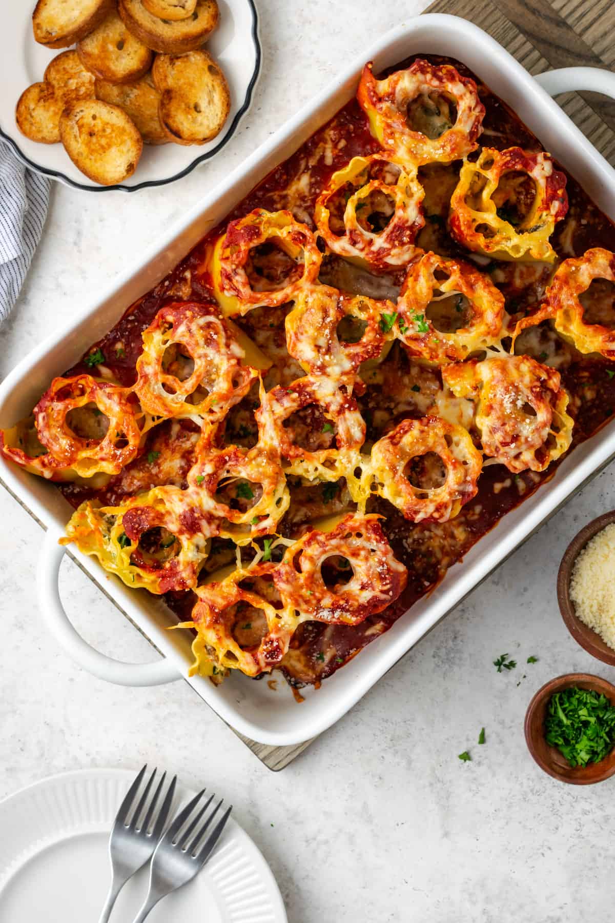 A large casserole dish with baked vegetable lasagna roll ups and a plate of toasted bread points to the side.