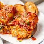Close up of veggie lasagna roll ups on a white plate with a fork resting to the side with a text overlay on the photo.
