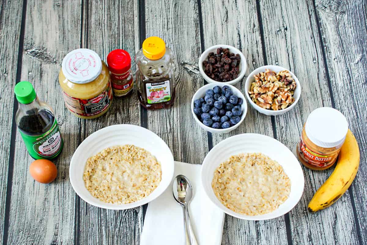 Two bowls of oatmeal made in the microwave surrounded by a variety of potential toppings.