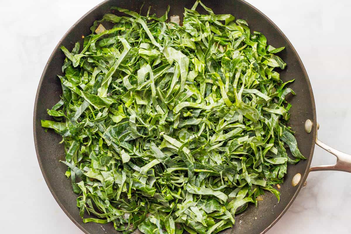 Thinly sliced collard greens in a large skillet before being cooked down.