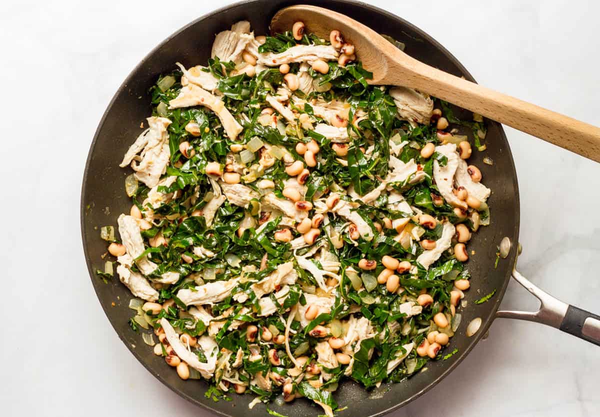 A large skillet with a mix of chicken, black eyed peas and collards.