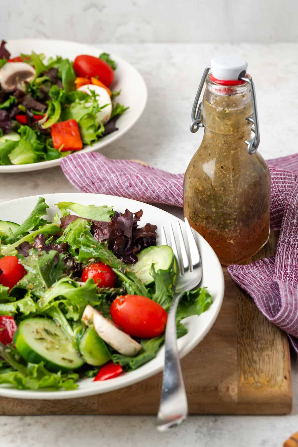 A jar of homemade salad dressing beside a bowl of salad set on a wooden cutting board.