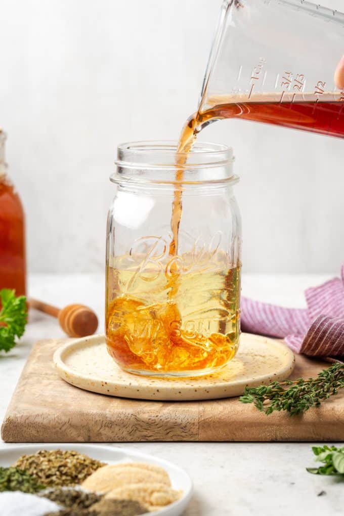 Vinegar being poured into a mason jar glass with olive oil in it.