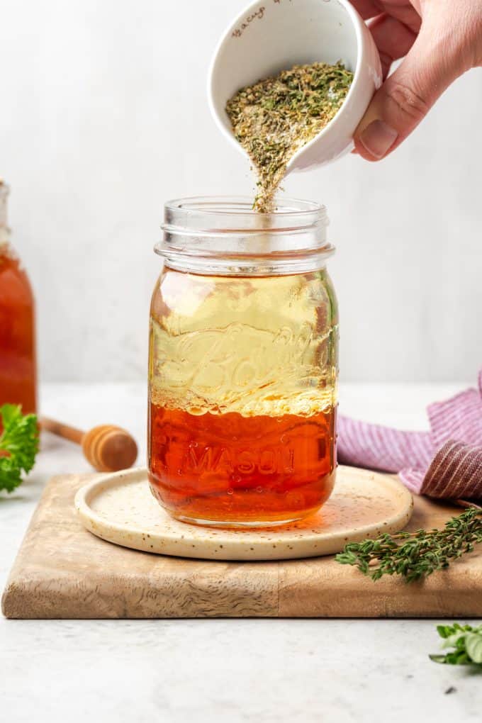 A mix of seasonings being added to a glass jar of oil and vinegar.