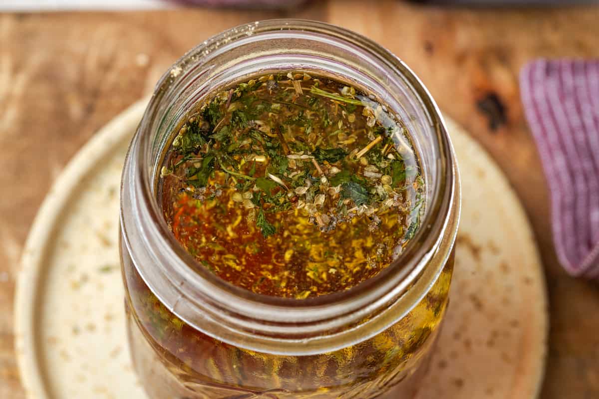 Close up of a homemade dressing with Italian seasonings in a glass jar.