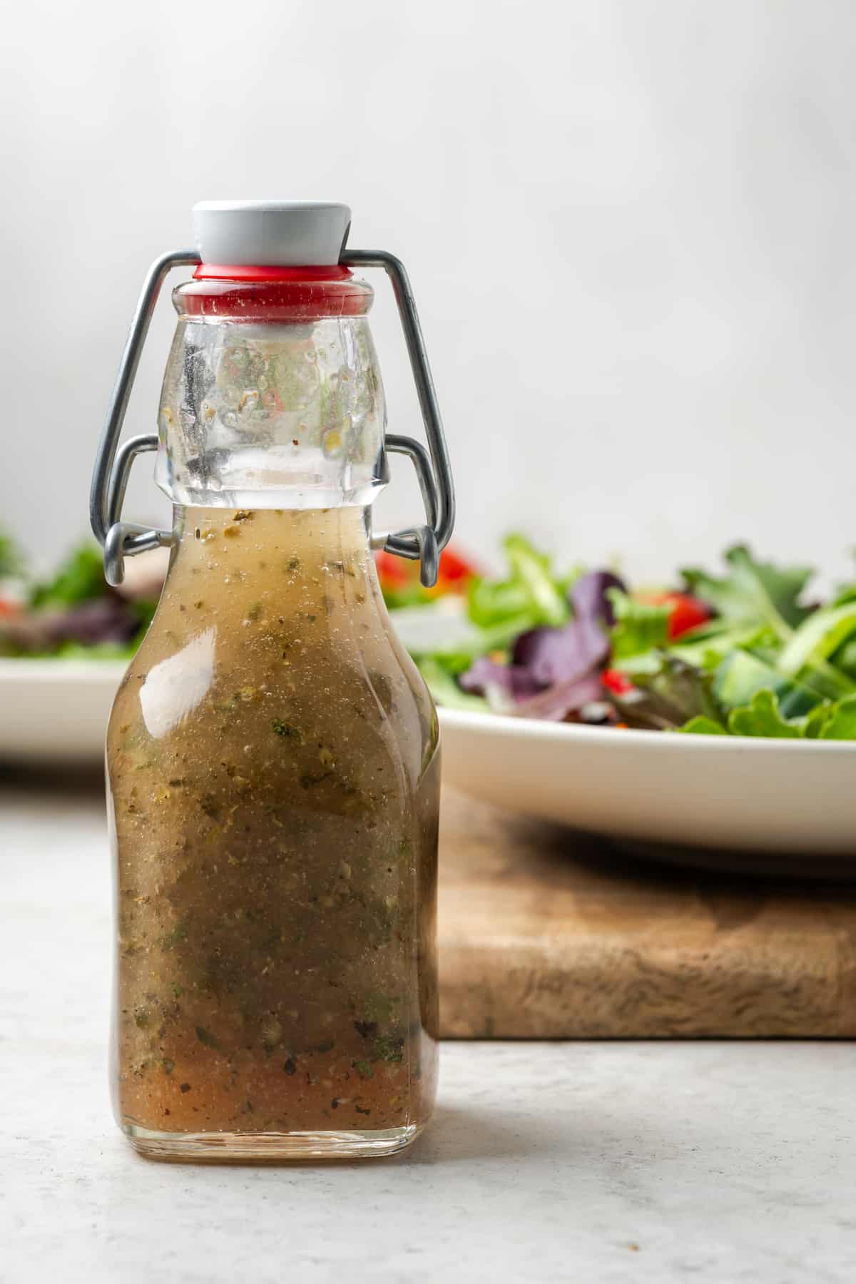 A dressing jar with homemade Italian dressing set in front of a couple of bowls of salad.