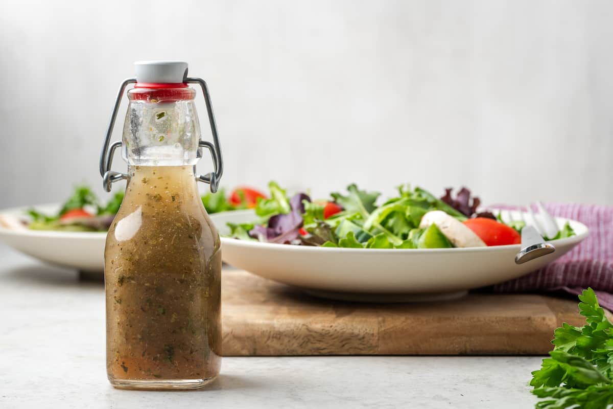 A glass dressing jar with homemade Italian dressing set in front of a couple of bowls of salad.