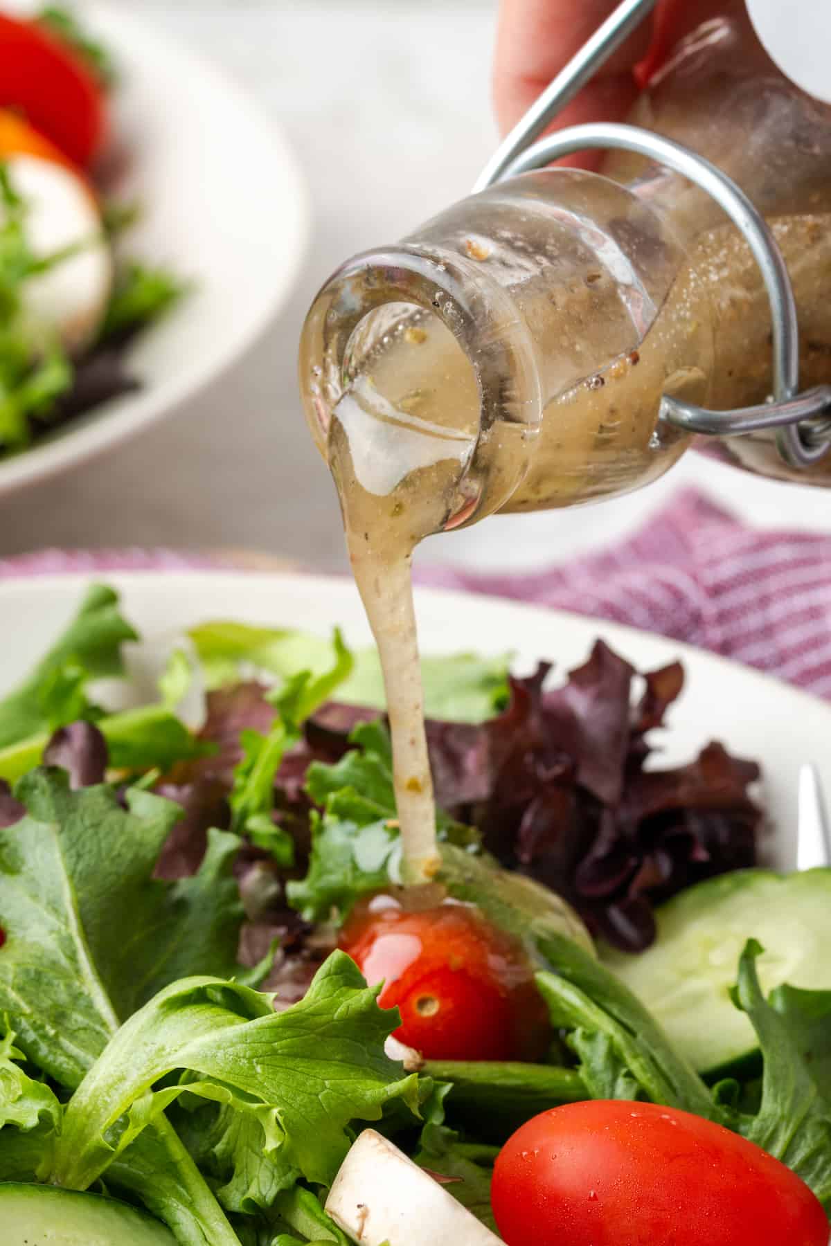 Italian dressing being poured over a salad of mixed greens with cucumber and tomato.