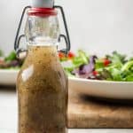 A dressing jar with homemade Italian dressing set in front of a couple of bowls of salad with a text overlay on the photo.