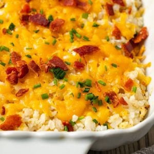 Close up of a baked cheesy cauliflower rice casserole in a white dish with bacon and green chives sprinkled on top.