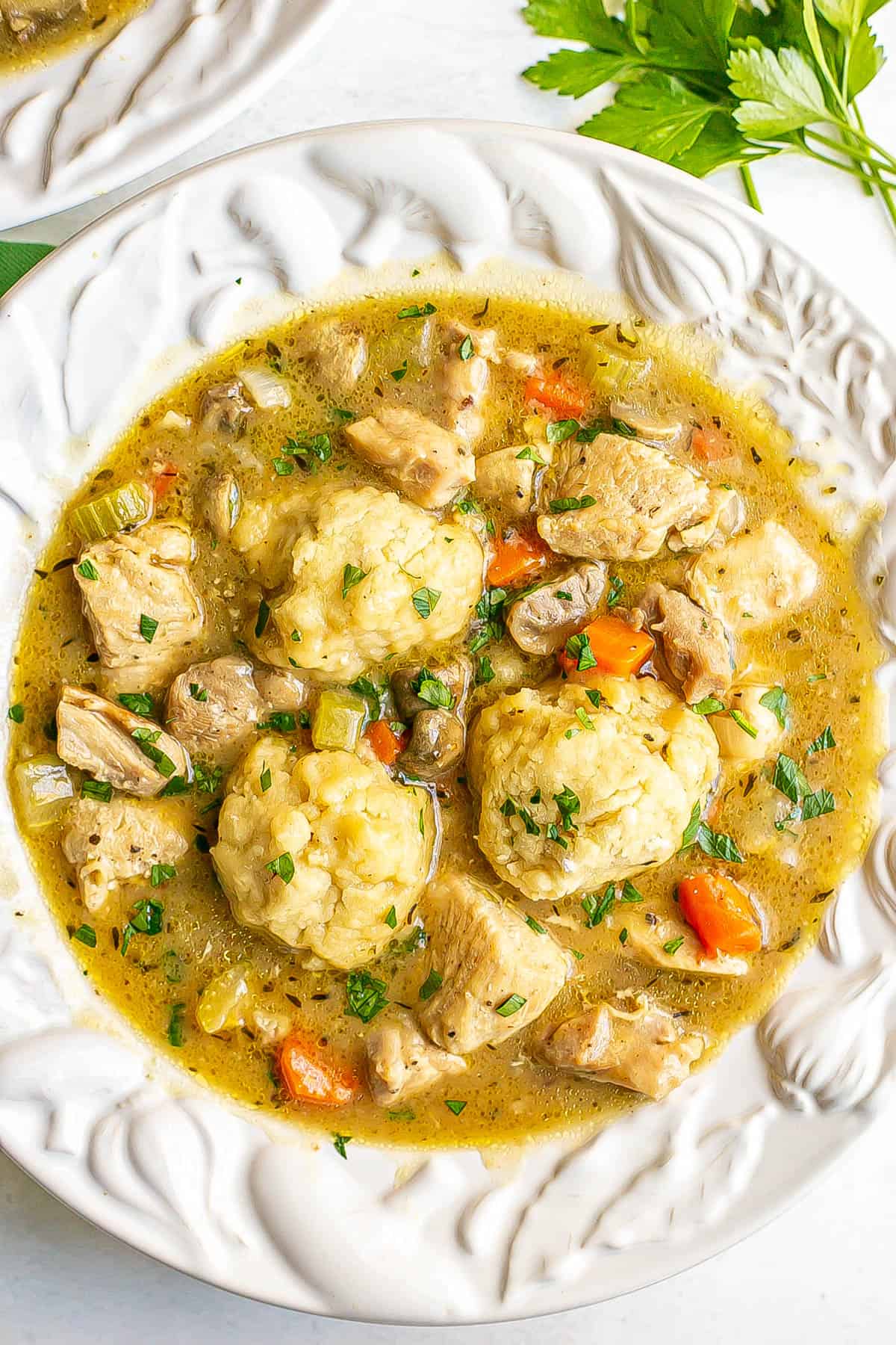 Chicken and dumplings with veggies served in a white decorative bowl.