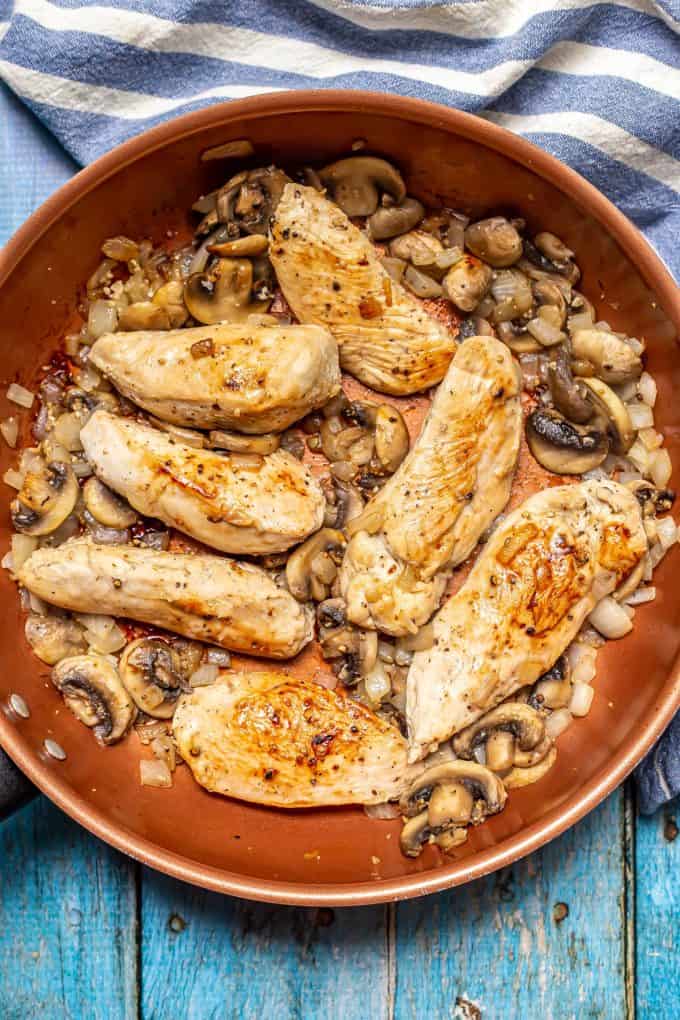 Seared chicken strips in a copper pan with sautéed onions and mushrooms.