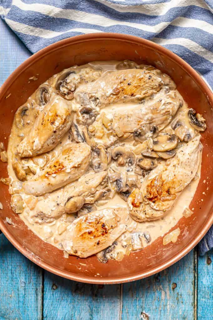 Seared chicken strips in a copper pan with sautéed onions and mushrooms and a creamy sauce.