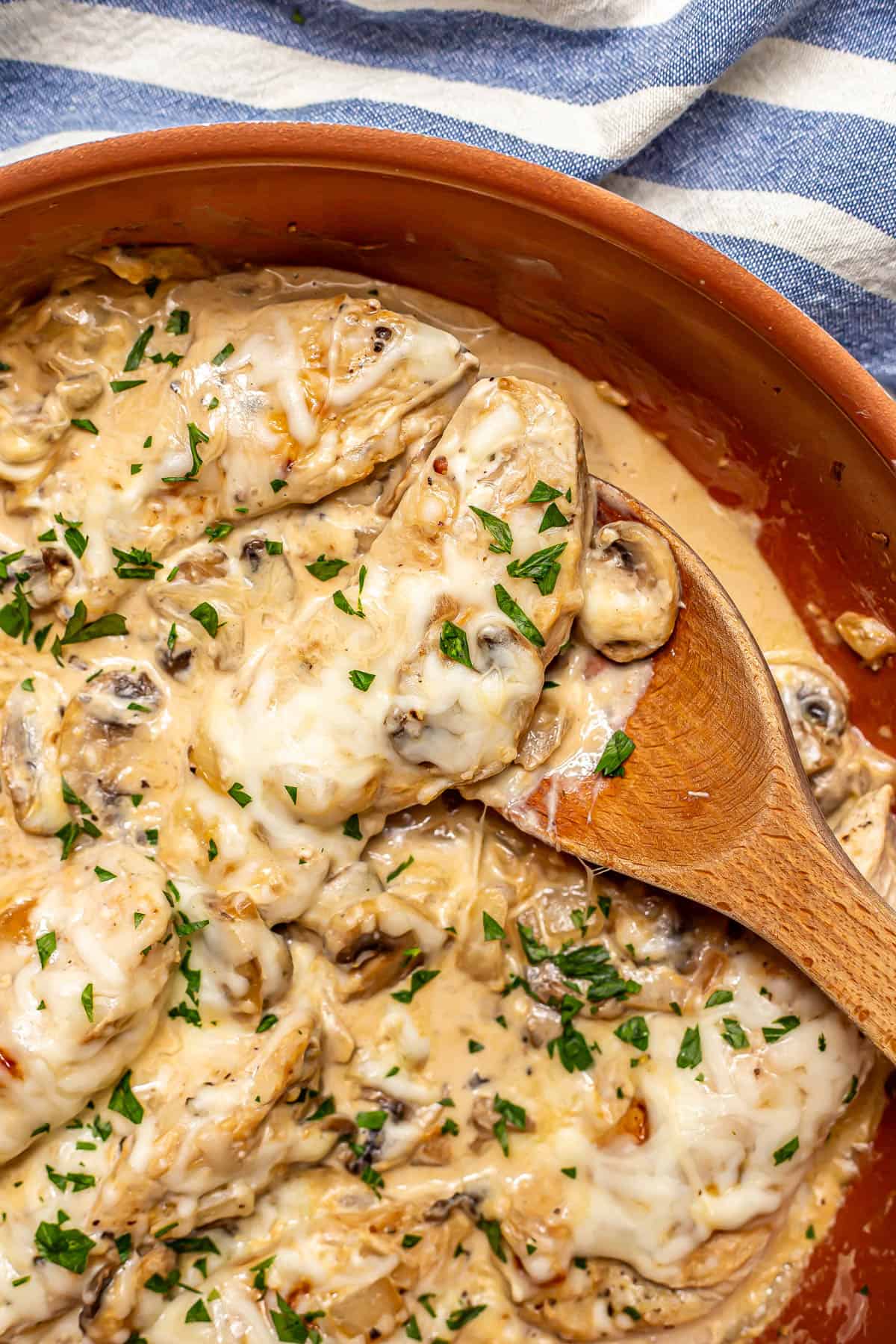 Close up of a wooden spoon scooping up some cream cheese chicken from a copper skillet.