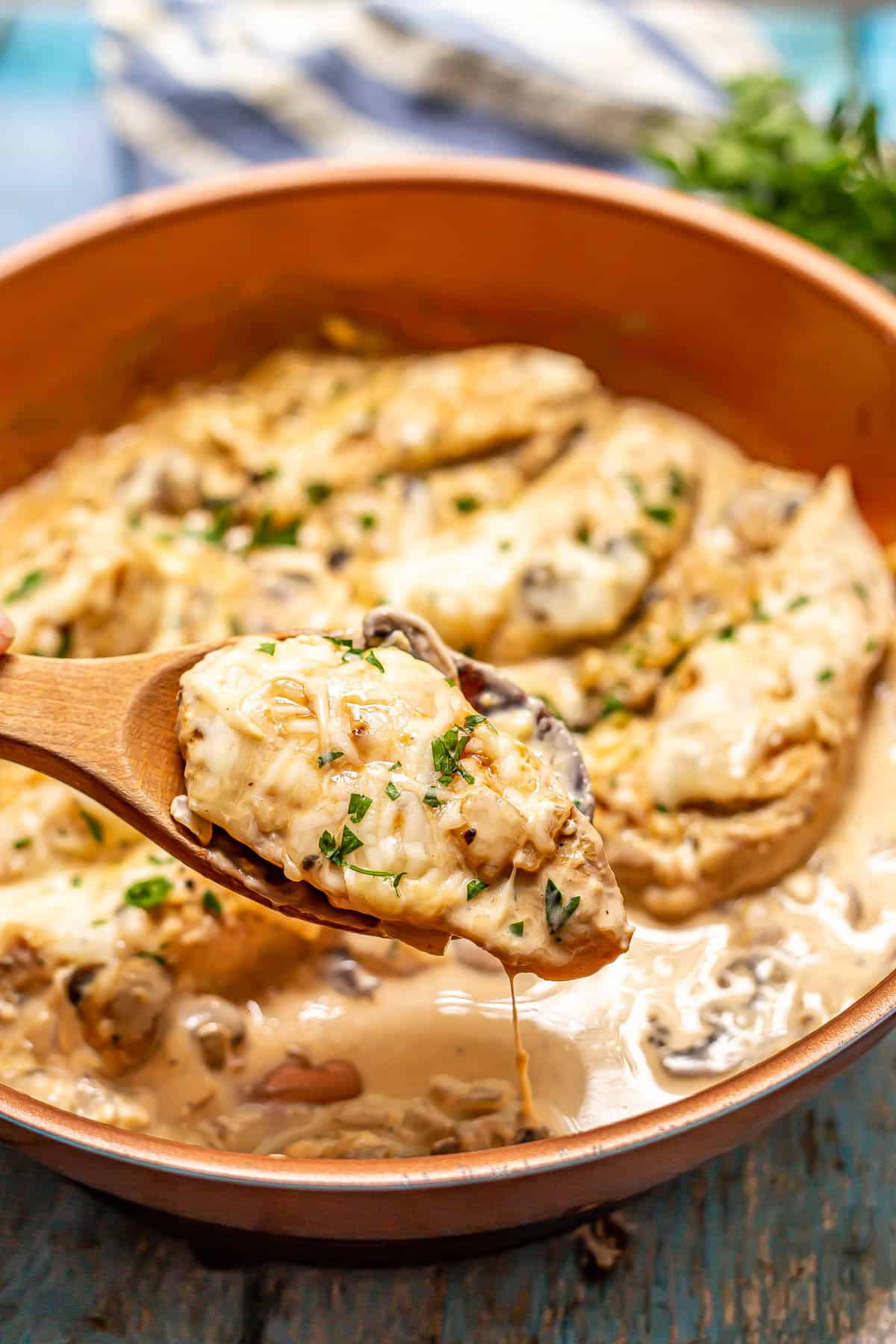 A wooden spoon lifting up a piece of creamy chicken from a large copper skillet.