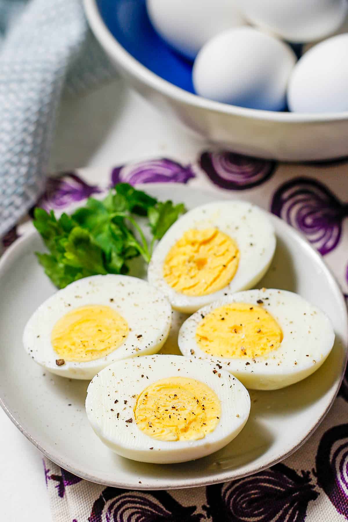 Two hard boiled eggs cut in half and served on a small plate with salt and pepper sprinkled on top and parsley to the side for garnish.