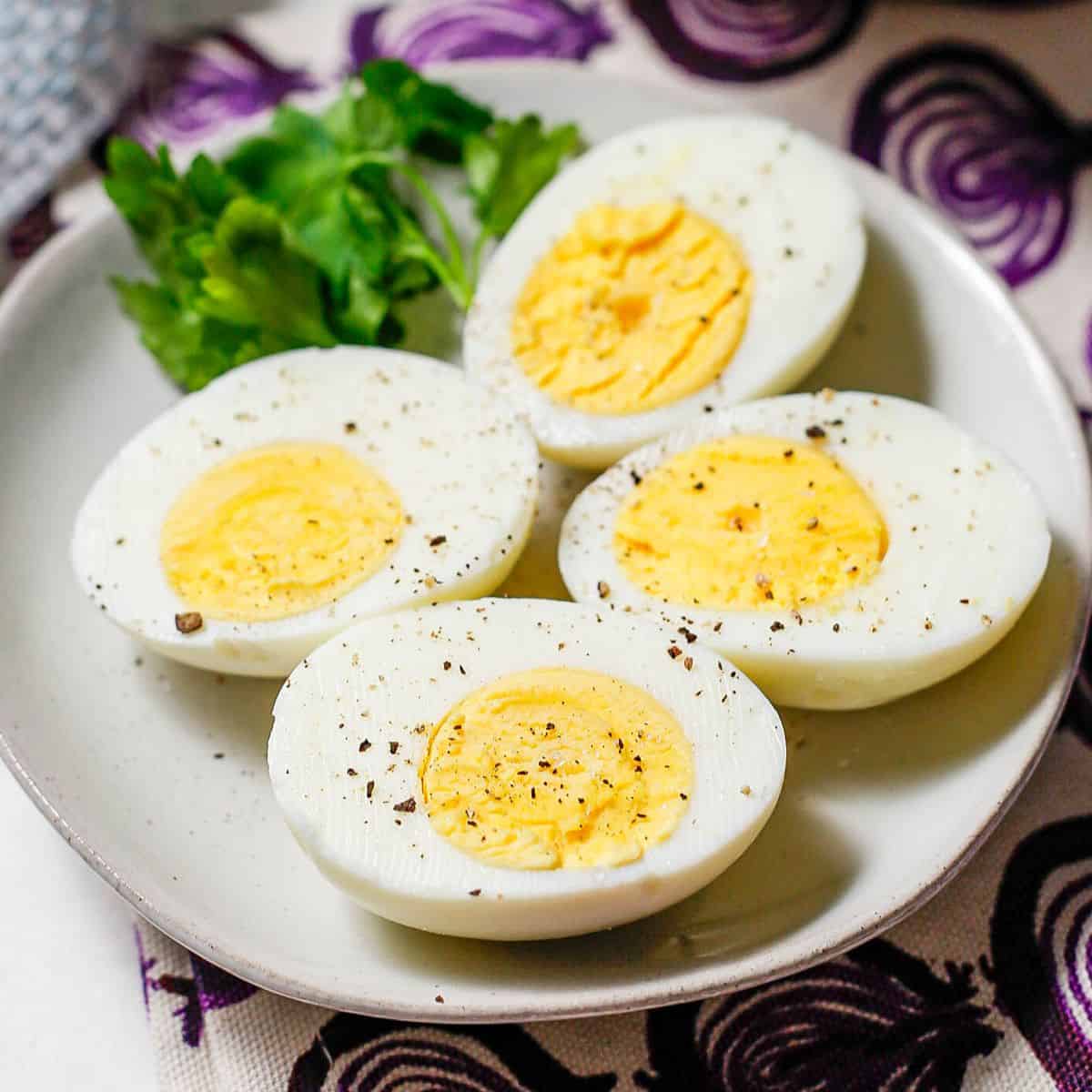 Close up of 2 hard boiled eggs cut in half and served on a small plate with salt and pepper sprinkled on top and parsley to the side for garnish.