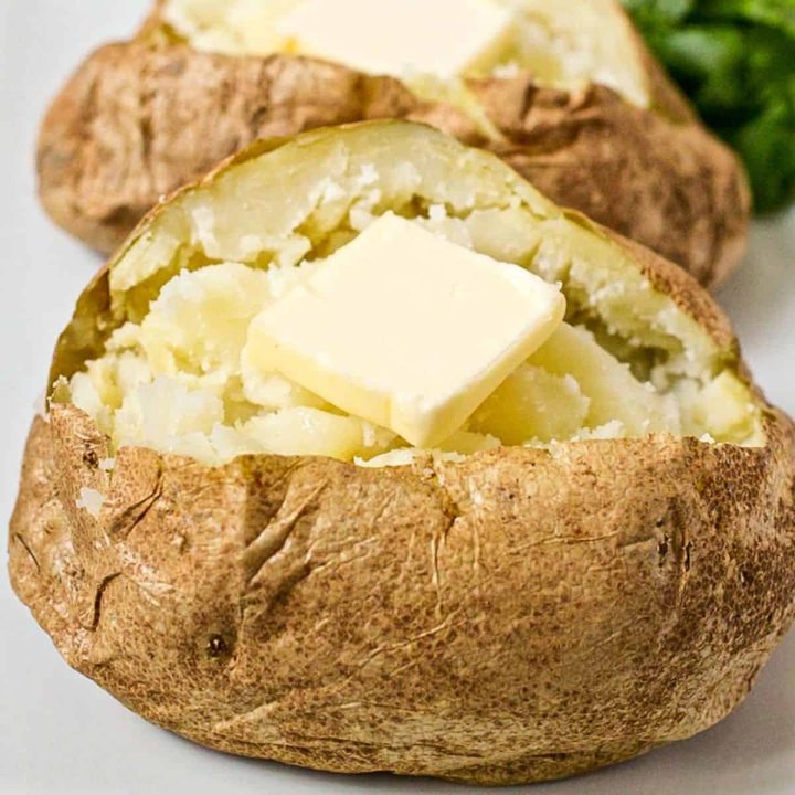 Close up of a microwave baked potato that's been opened and fluffed and topped with a pat of butter.