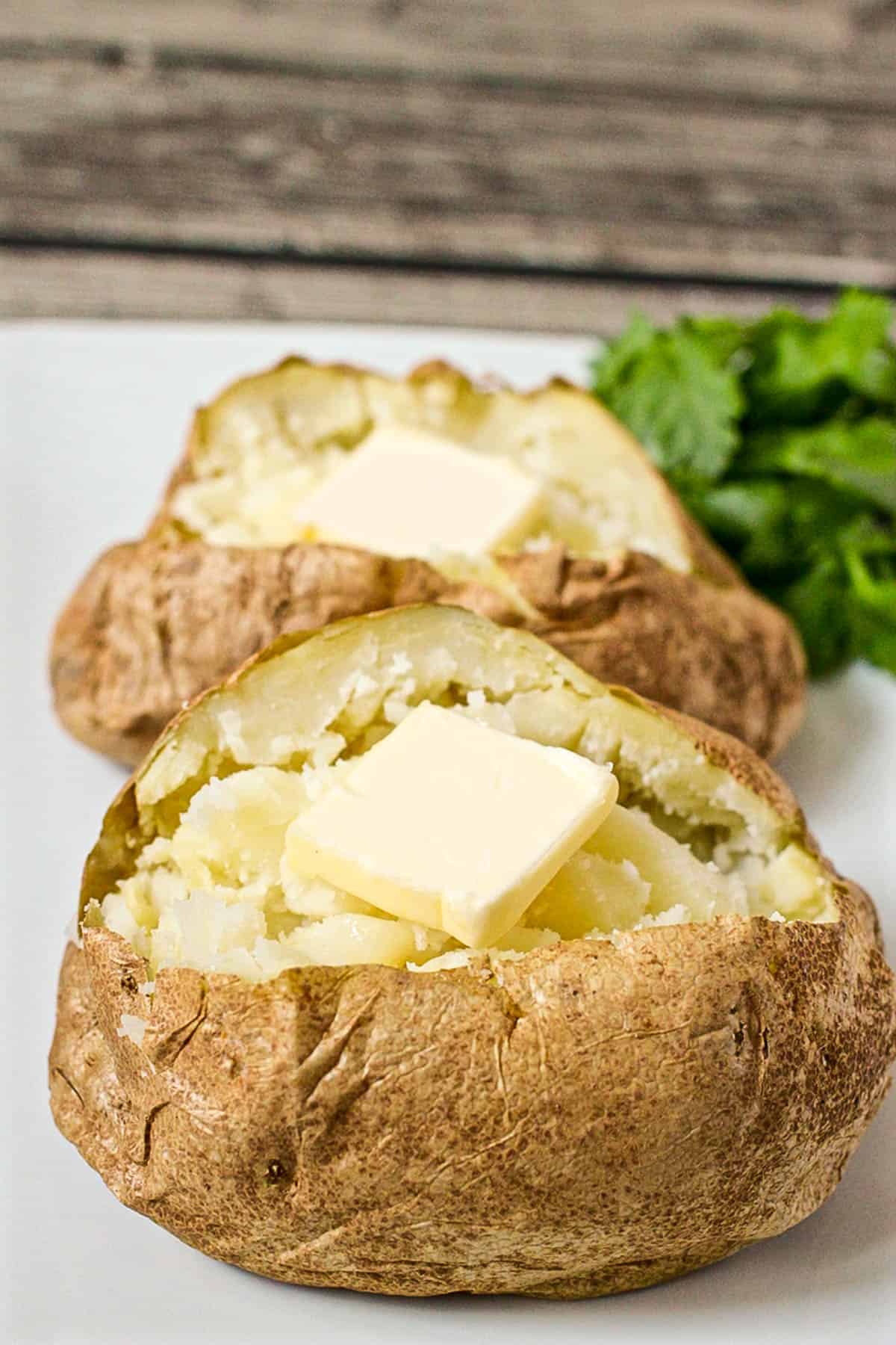 Two microwave baked potatoes on a white platter with pats of butter in each one.