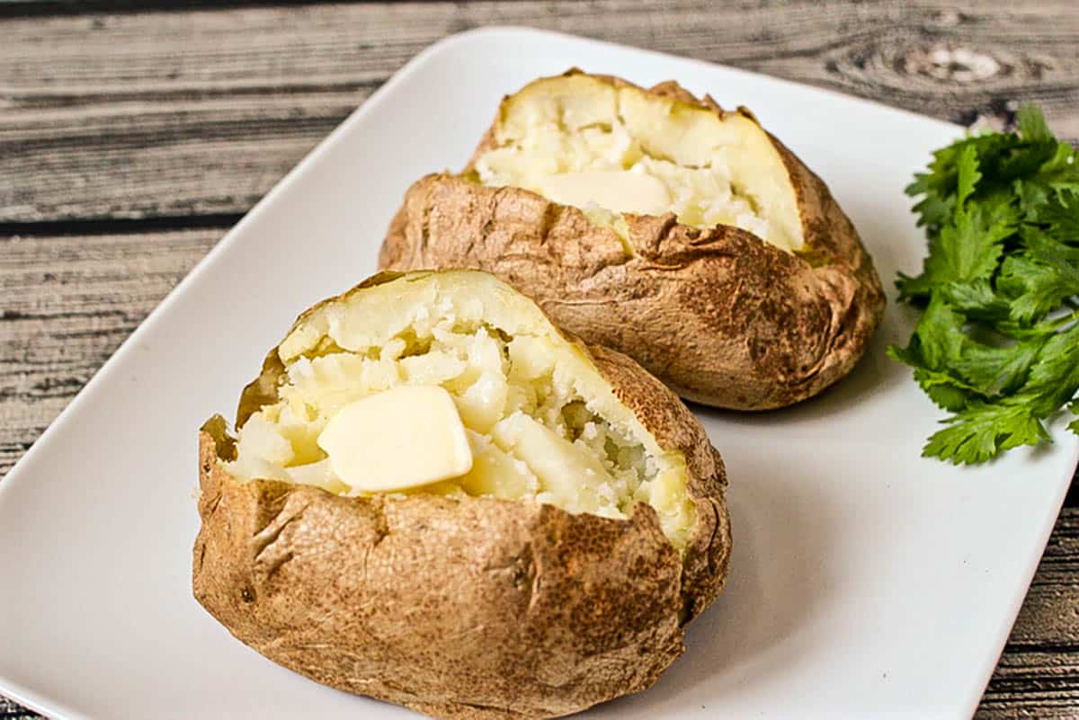 Two quick cooked russet potatoes opened and fluffed and topped with a pat of butter.