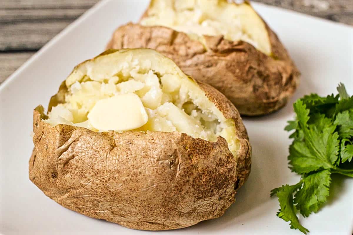 Close up of two cooked russet potatoes opened and fluffed and topped with a pat of butter.