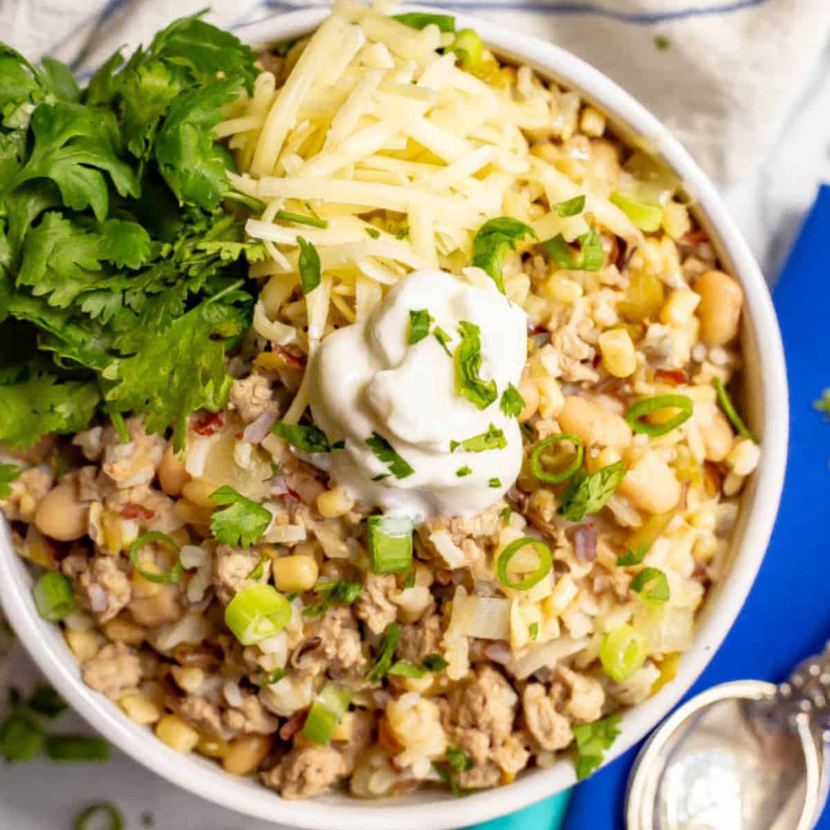 Close up of a bowl of white turkey chili with wild rice and great Northern beans with chili toppings arranged on top.