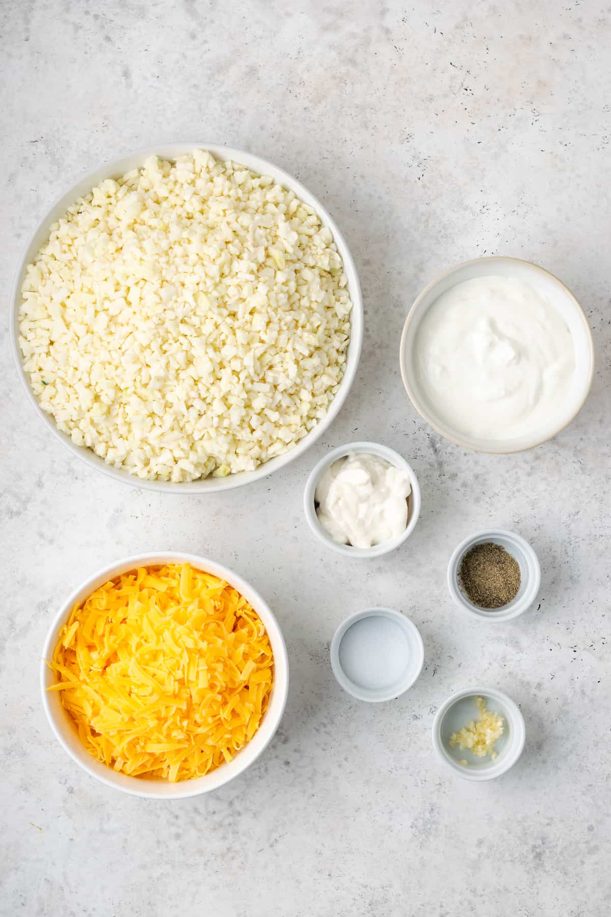 Ingredients laid out in separate bowls for a cheesy cauliflower rice.