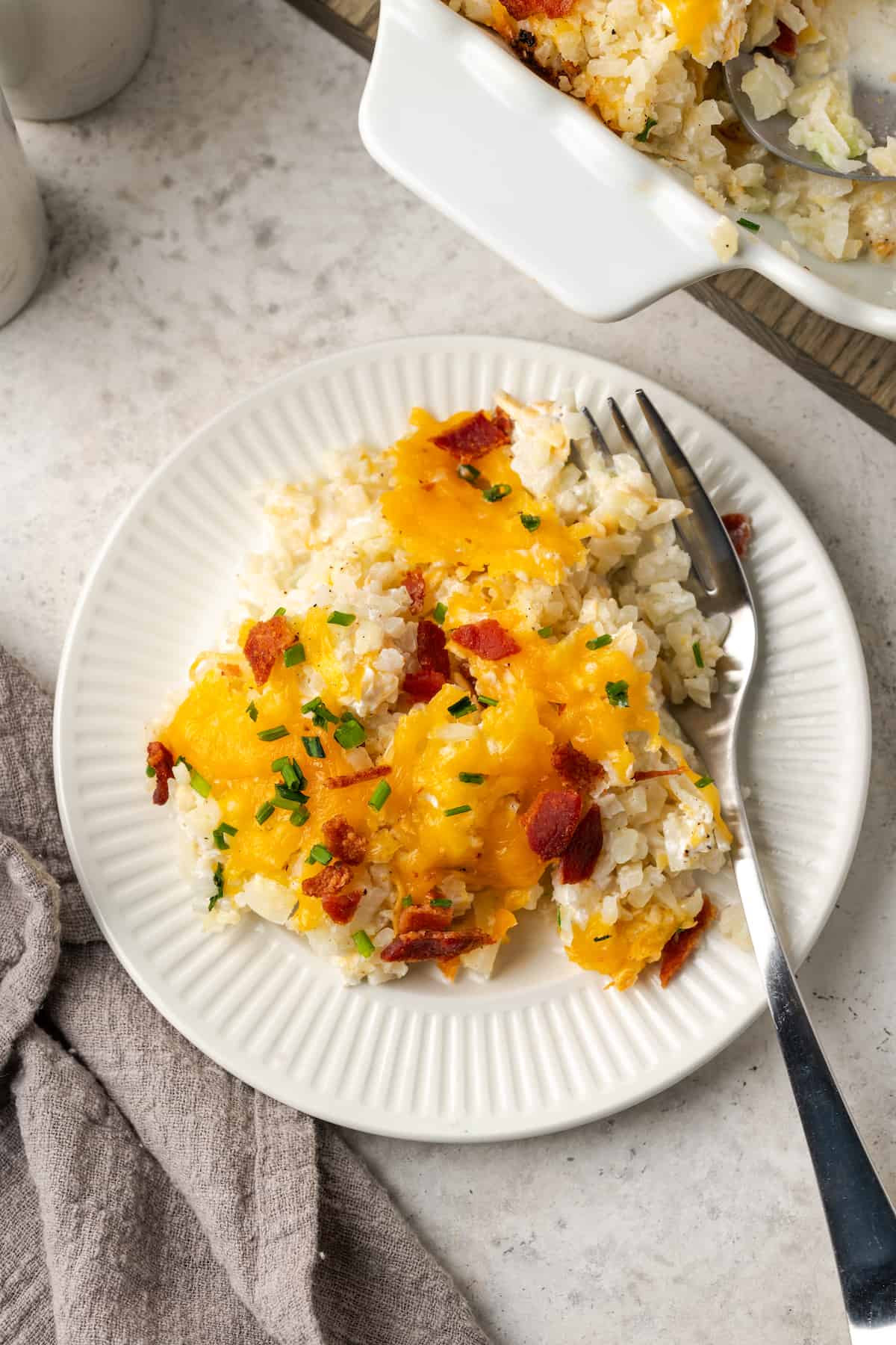 A fork resting alongside a serving of cheesy cauliflower rice served on a white plate.