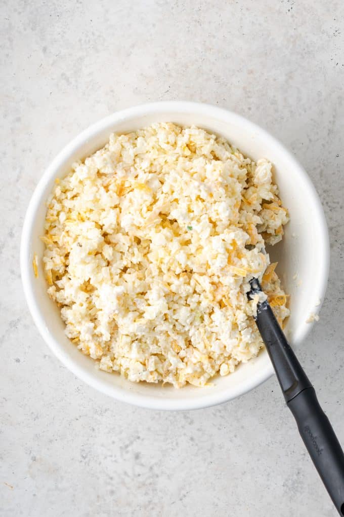 A creamy, cheesy cauliflower rice mixture in a mixing bowl with a spoon resting in it.