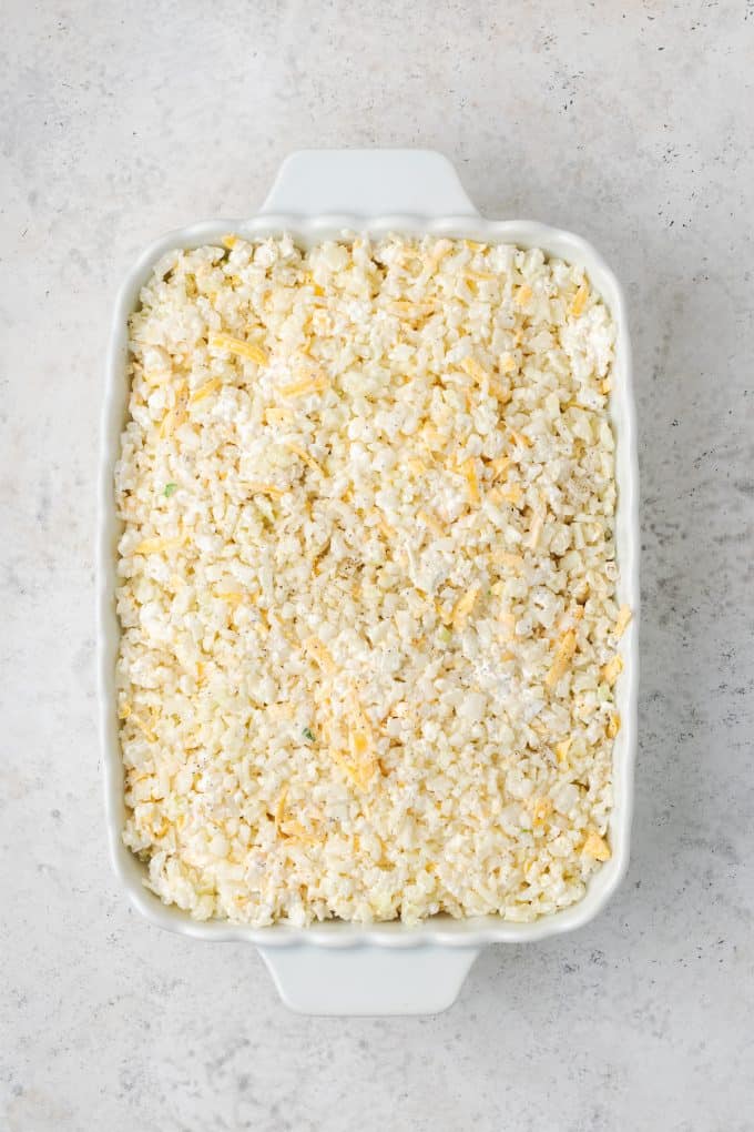 A cauliflower rice mixture spread out in a baking pan before being cooked.